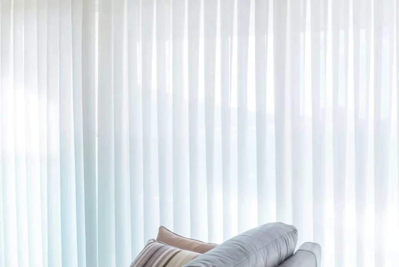 Translucent white vertical blinds drawn across a living room window behind a sofa
