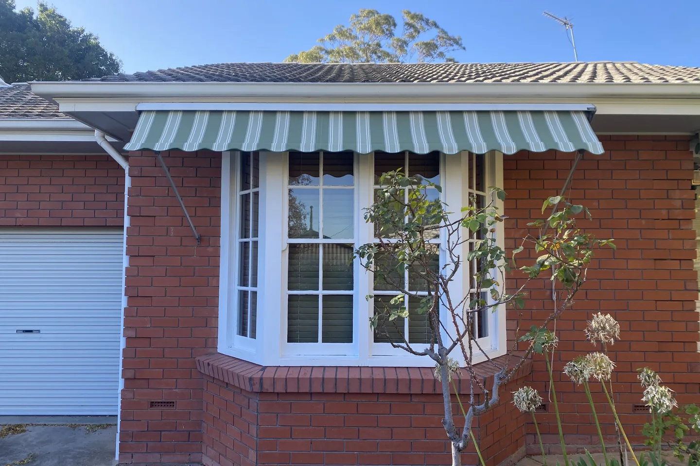 Striped auto guide awning angled out from a bay window on its locking arms