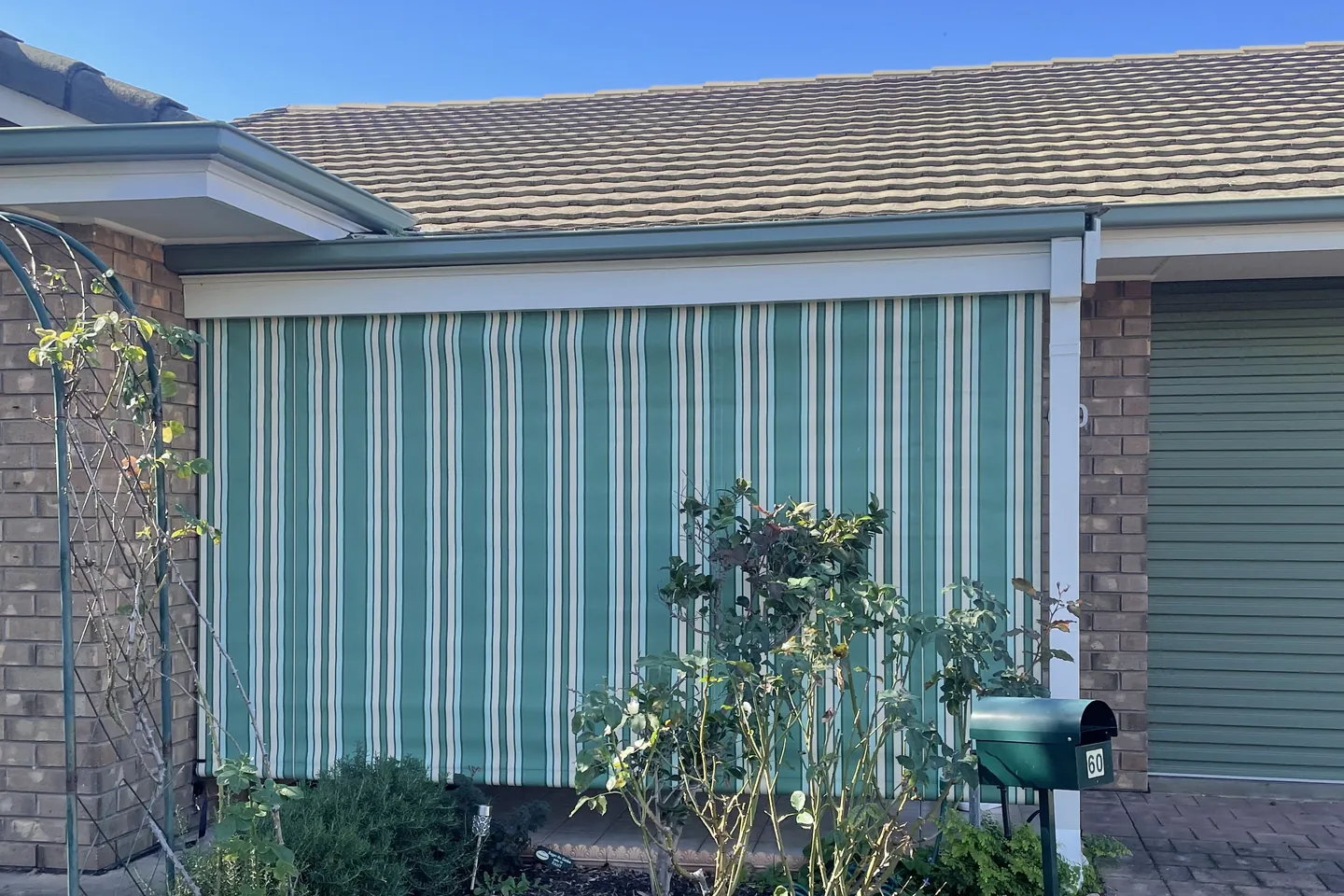 Wide green striped auto guide awning lowered across the front of a brick home