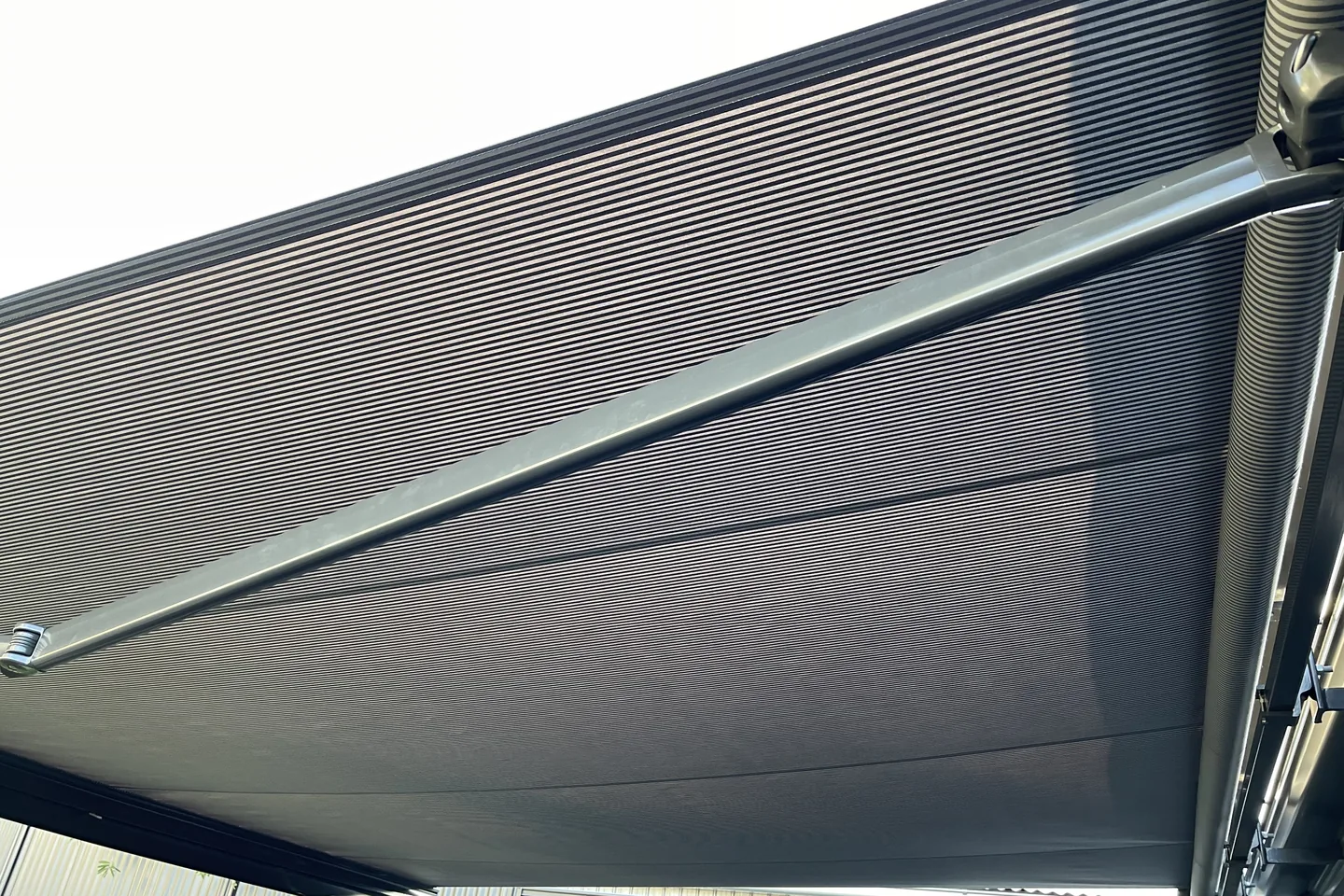 Underside of an extended grey folding arm awning showing the arm and front bar