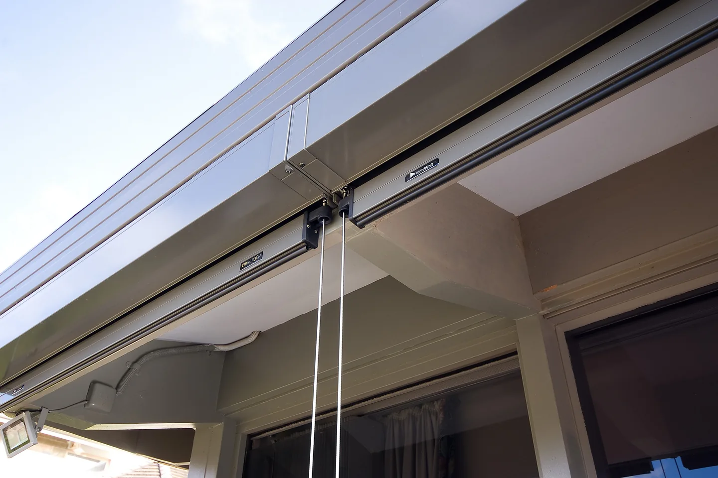 Headbox of a wire guided blind under the eave, with the guide wires dropping below