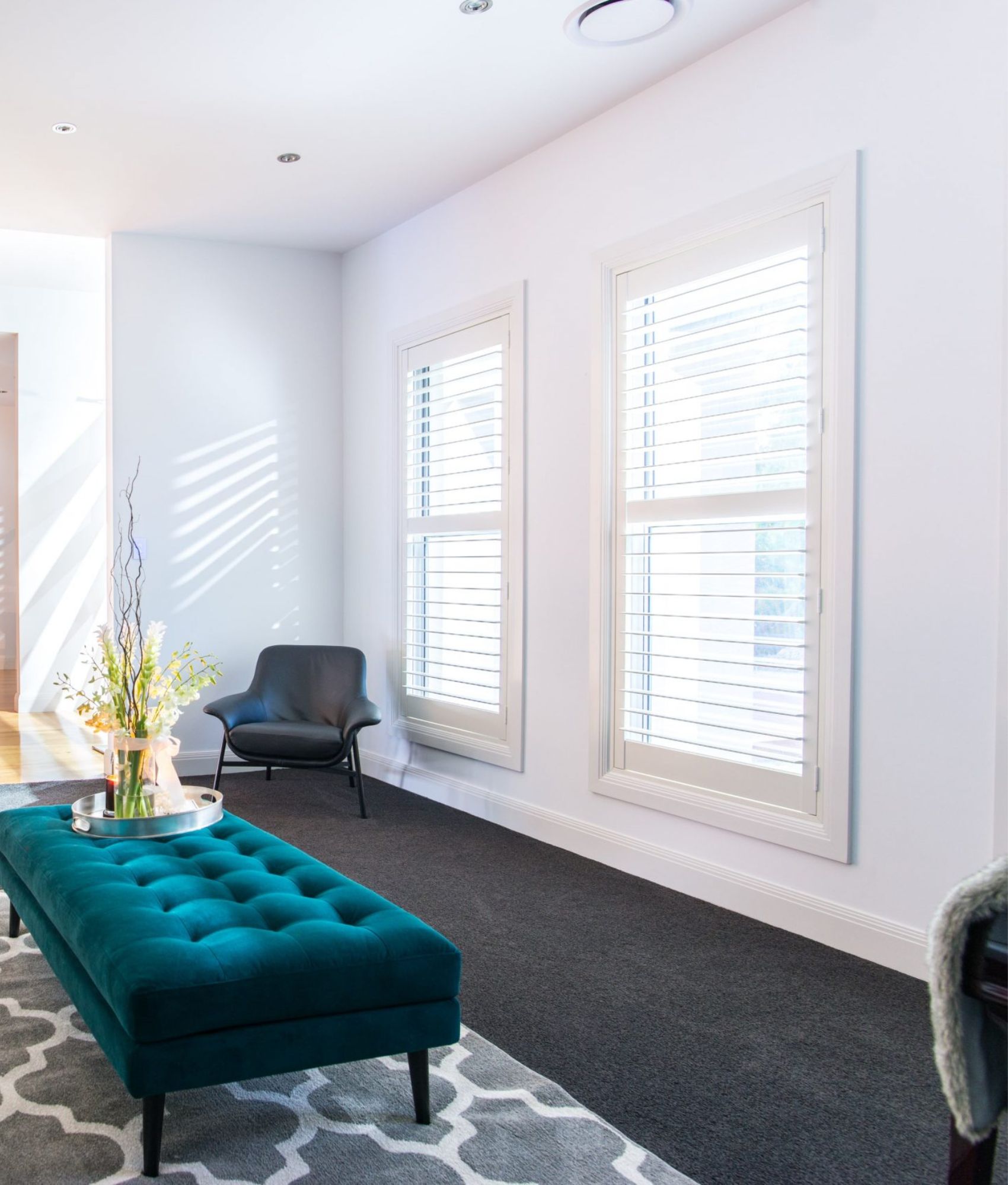White plantation shutters beside a teal ottoman