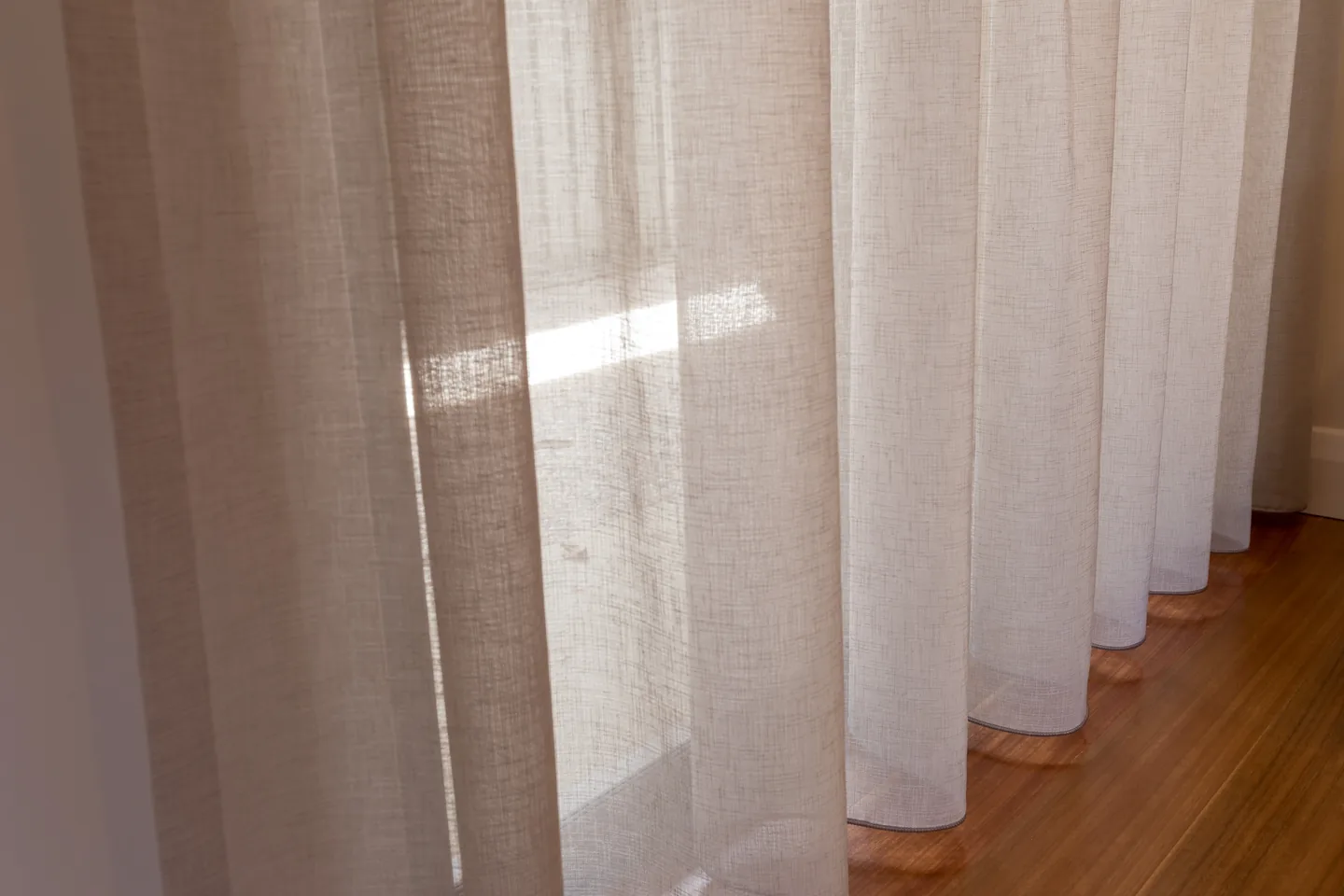 Linen-look sheer curtain folds catching daylight above a timber floor