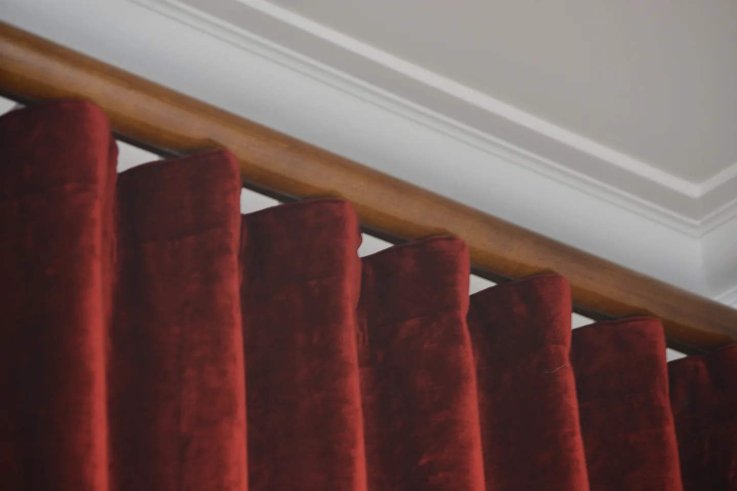 Deep red velvet pleats hanging from a timber curtain rod