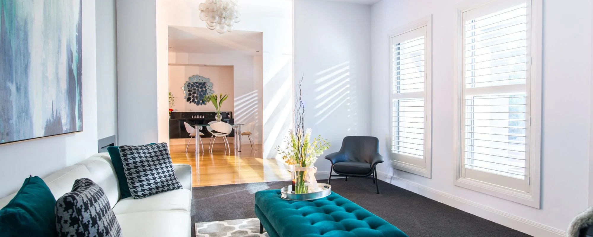 White plantation shutters in a bright living room with a teal ottoman
