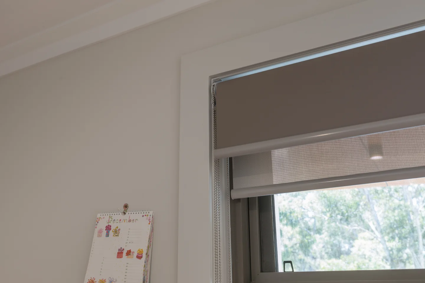 Dual roller blind with a dark blockout blind raised above a lowered light sunscreen blind