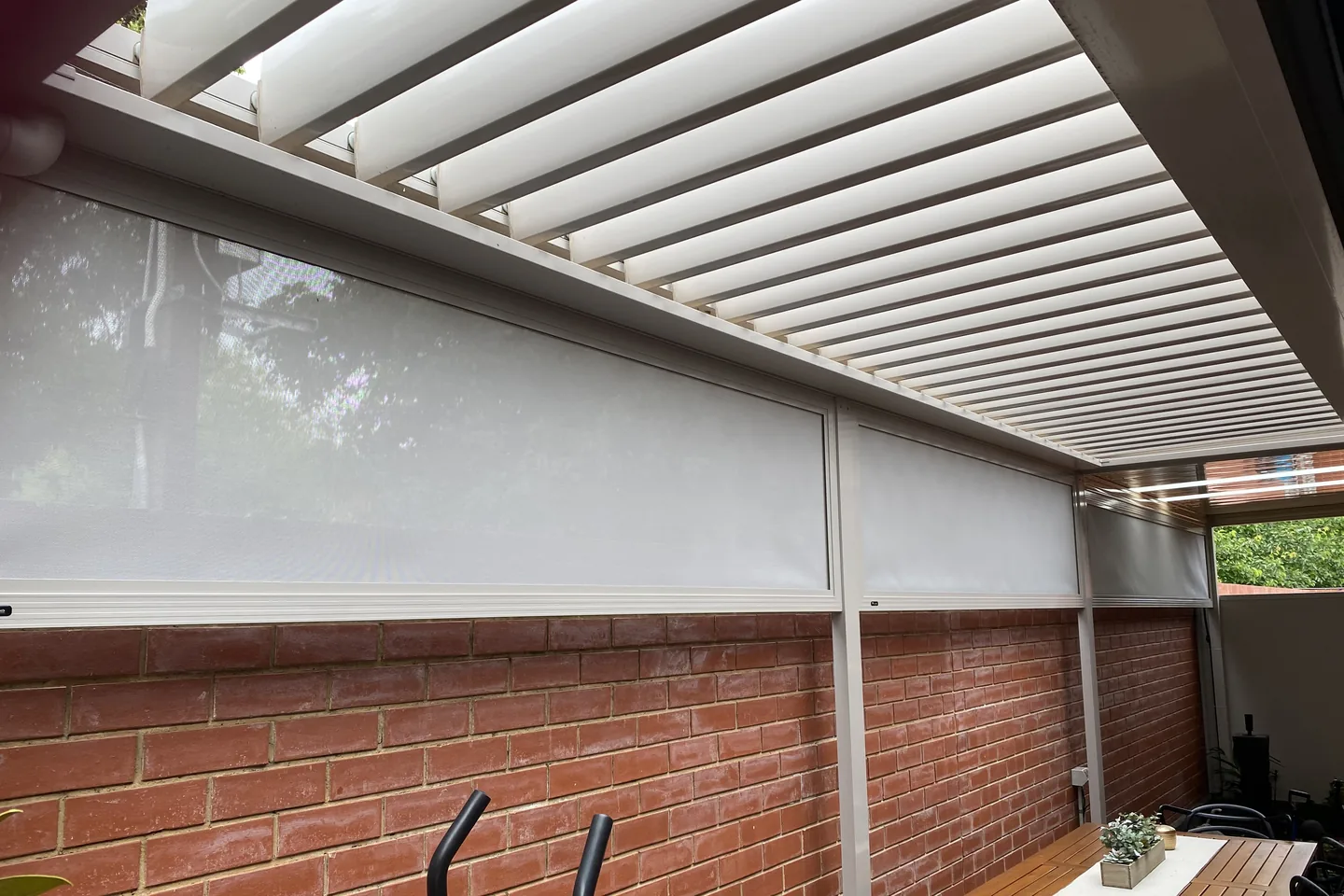 Mesh infill panels running the length of a pergola beside an outdoor table
