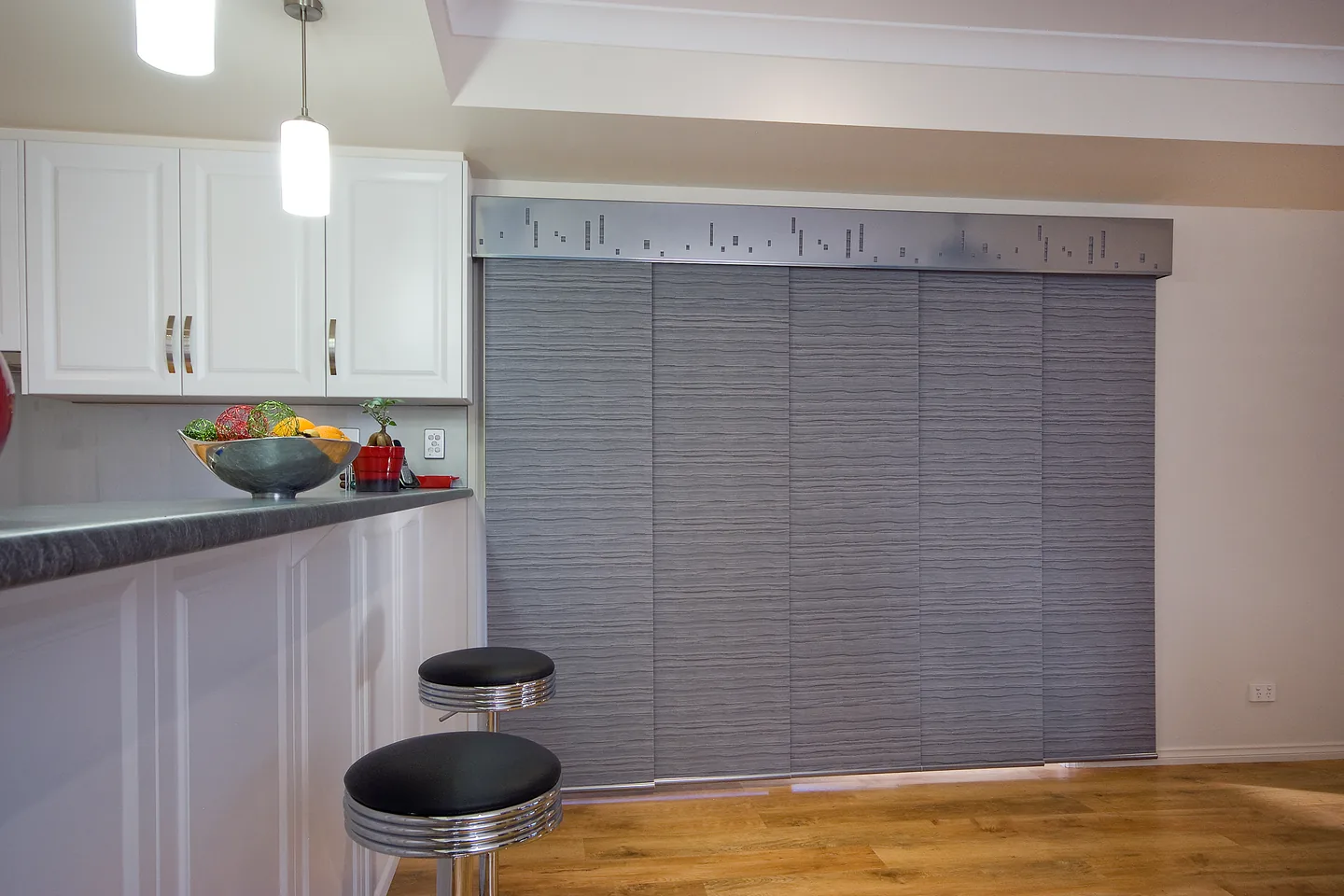 Kitchen bench and stools beside grey panel glide blinds drawn across a sliding door