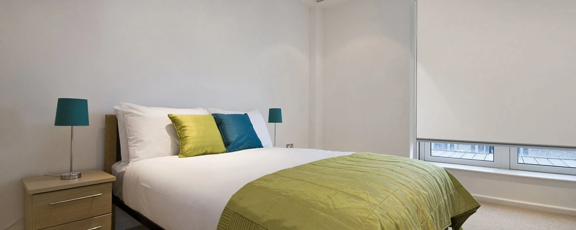 Bedroom with a pale interior blind partly lowered over a large window