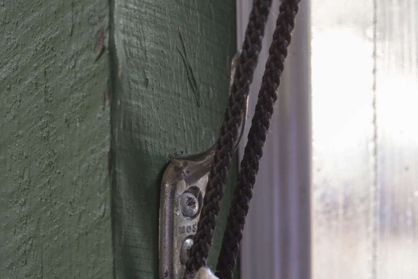 Cord tied off on a metal cleat on a green verandah post beside a clear blind