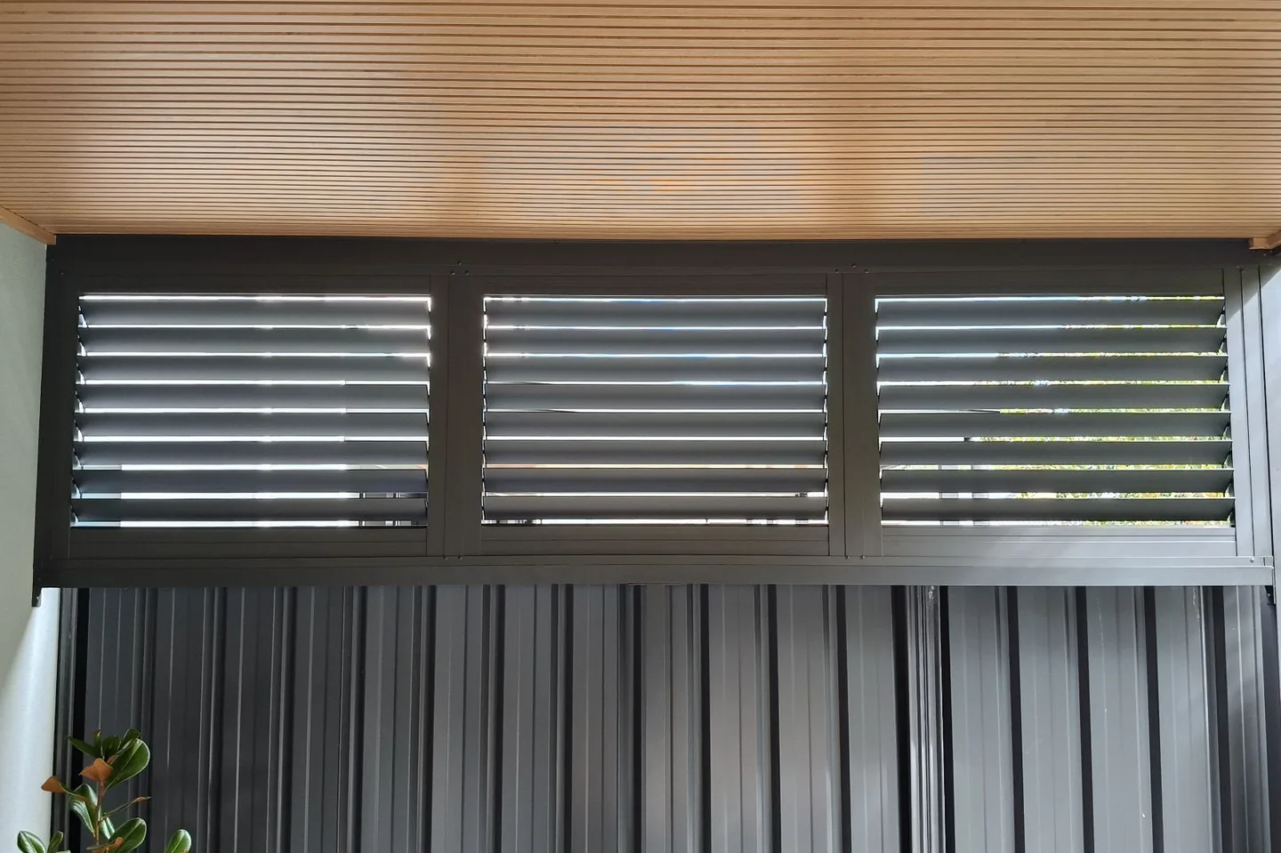 Dark framed shutters fitted across an opening above a steel fence under a timber ceiling