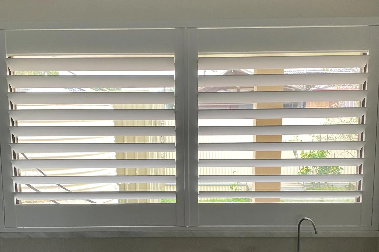 The same kitchen window with the plantation shutter louvres tilted open to the garden outside