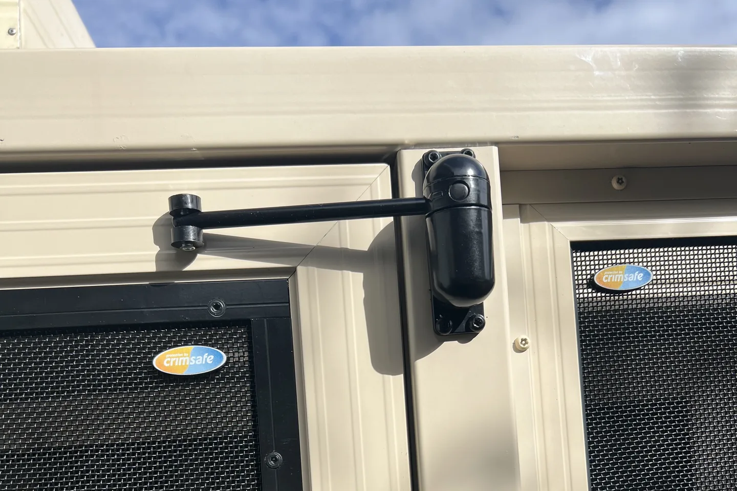 Door closer fitted to the top of a cream-framed mesh security door, with the Crimsafe badge on the mesh