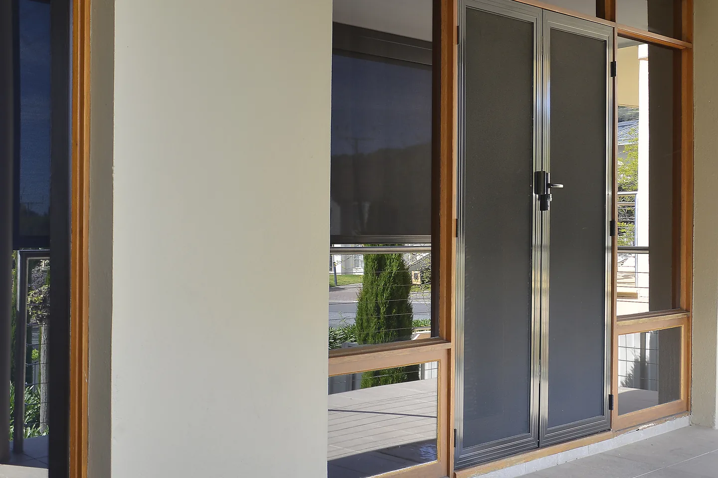 Row of timber-framed windows and doors along a covered balcony, each screened with dark Crimsafe mesh