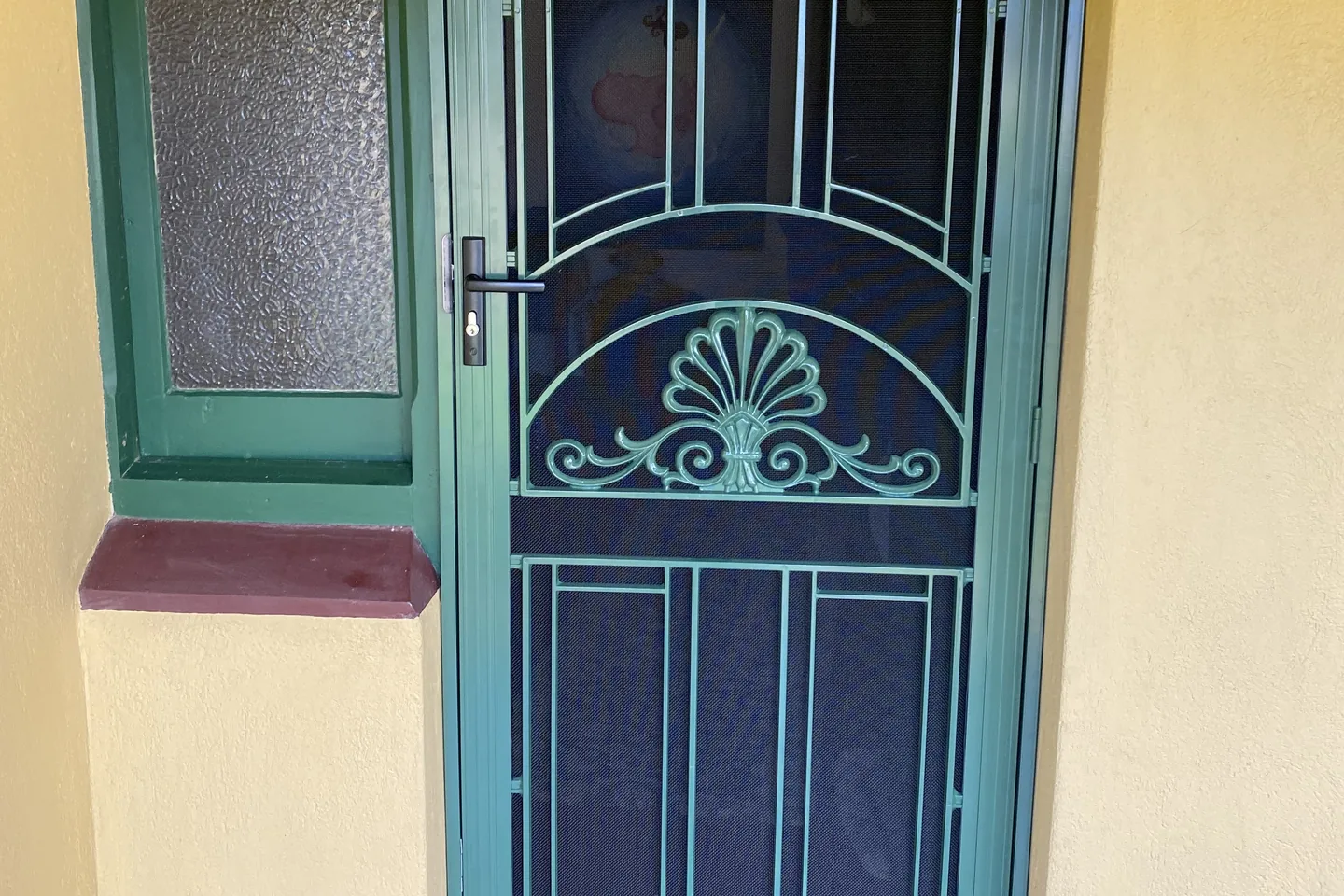 Green decorative security door with a fan motif, beside a matching green window frame